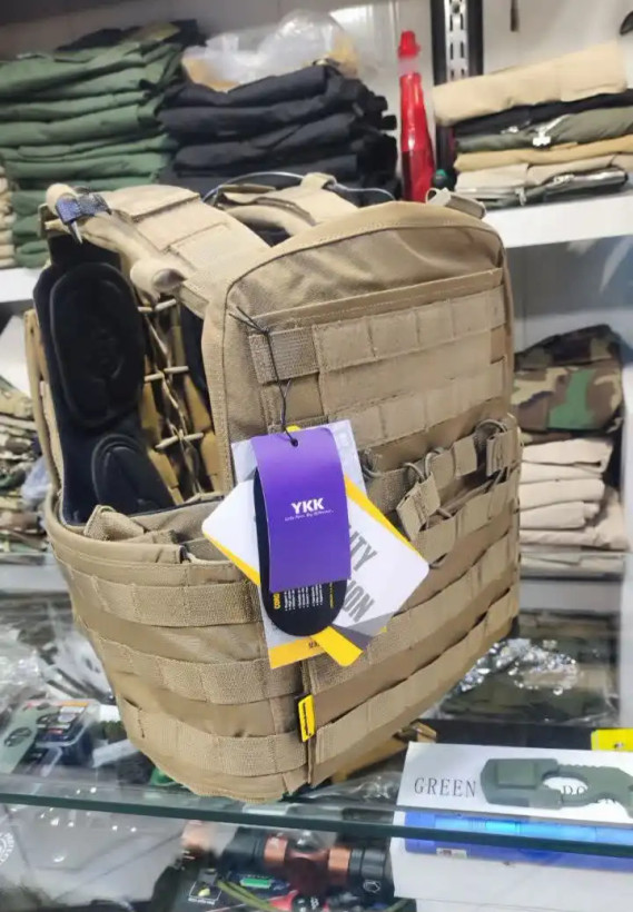 نمایش جلیقه تجهیزات نظامی رنگ خاکی با جیب جلو، سیستم MOLLE و تگ CORDURA در فضای فروشگاه.